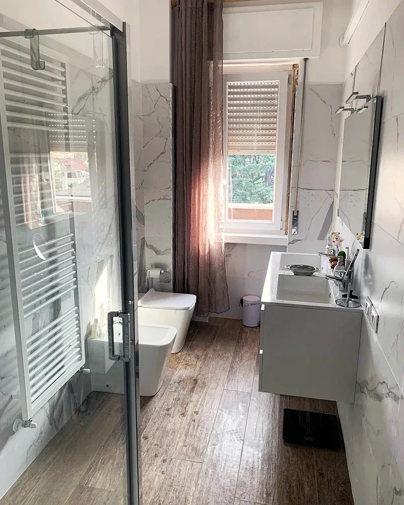 Lo stesso bagno con nuovi rivestimenti, box doccia e mobile lavabo bianco